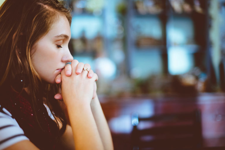 Photo de profil d'une jeune fille les yeux fermés  portant ses 2 mains à sa bouche en signe de prière