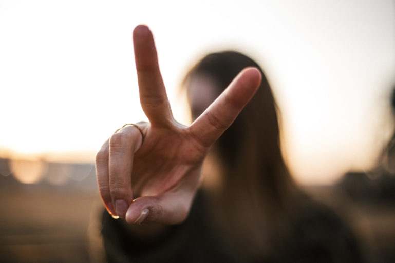 Photo de face d'une jeune fille faisant un V, le signe de la victoire avec ses doigts